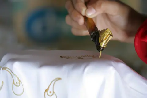 Tangan menorehkan malam cair dengan canting pada kain putih untuk membuat batik tulis