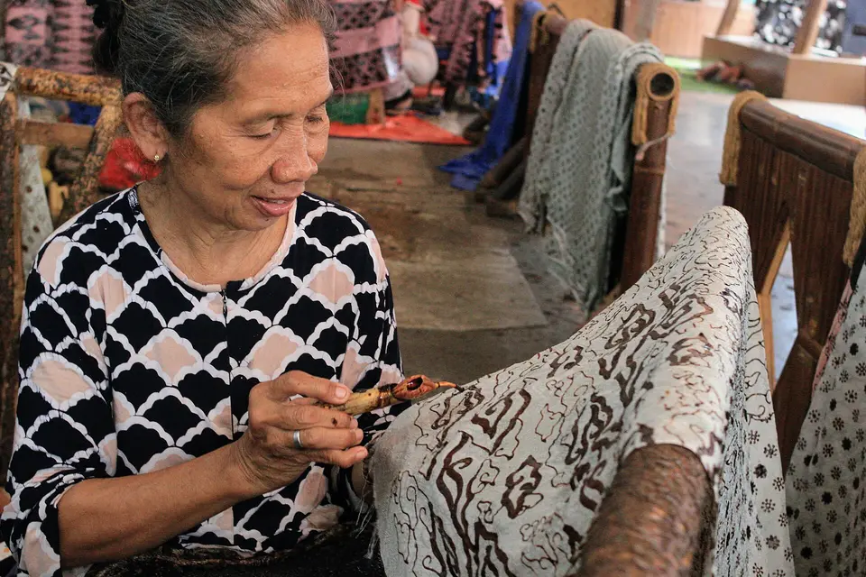 Seorang perajin perempuan menorehkan malam dengan canting pada kain batik tulis di bengkel batik